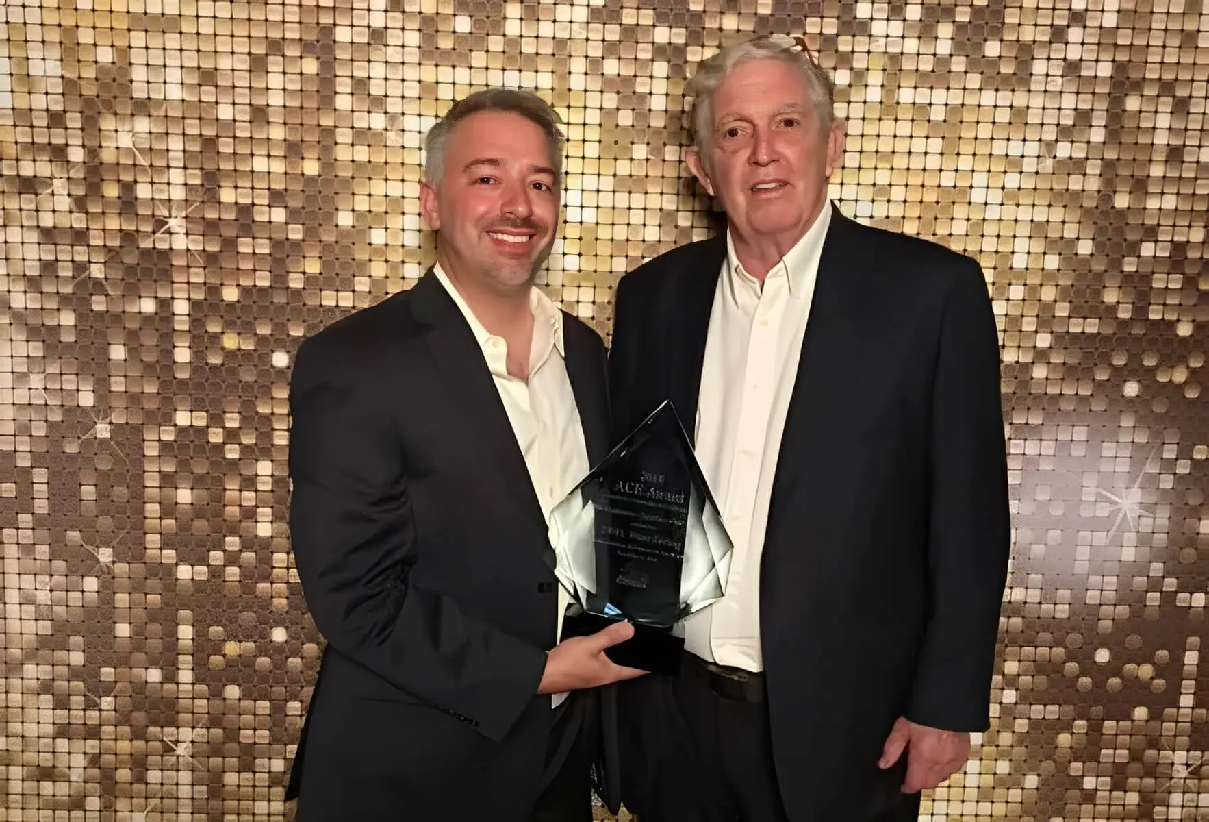 Two men holding a glass award together.